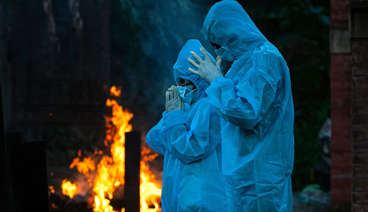 Seorang anak laki-laki berusia 9 tahun (kiri) dengan alat pelindung diri berdoa selama kremasi ayahnya yang meninggal karena virus corona COVID-19 di Gauhati, India pada 28 September 2020. (AP Photo/Anupam Nath)