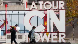Seorang pria yang memakai masker berjalan melewati papan nama CN Tower di Toronto, Kanada, pada 3 Oktober 2020. CN Tower kembali ditutup untuk umum pada Sabtu (3/10) di tengah melonjaknya kasus COVID-19. (Xinhua/Zou Zheng)