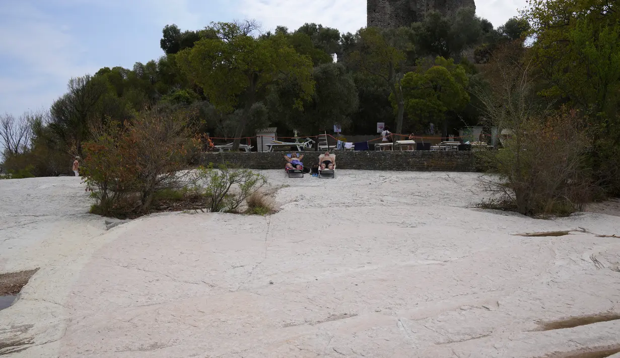 Orang-orang berjemur di semenanjung Sirmione, di danau Garda, Italia, Jumat (12/8/2022). Permukaan air Danau Garda telah turun secara kritis menyusul kekeringan parah yang mengakibatkan munculnya bebatuan di sekitar Semenanjung Sirmione. (AP Photo/Antonio Calanni)