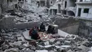 Keluarga Tareq Abu Ziad menunggu waktu berbuka puasa di tengah reruntuhan rumah mereka yang hancur setelah serangan militer pasukan pemerintah dan sekutunya di Kota Ariha, Provinsi Idlib, Suriah, Senin (4/5/2020). Muslim Suriah melewati Ramadan tahun ini masih dalam kondisi perang. (AAREF WATAD/AFP)