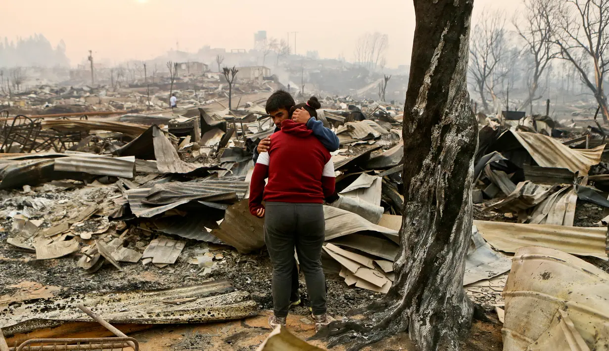Juan Vega memeluk putrinya sambil meratapi rumah mereka yang hangus dilalap api di Santa Olga, Chile, (26/1). Sebanyak 6.000 warga berhasil menyelamatkan diri dari kebakaran hebat tersebut. (AP Photo/Esteban Felix)