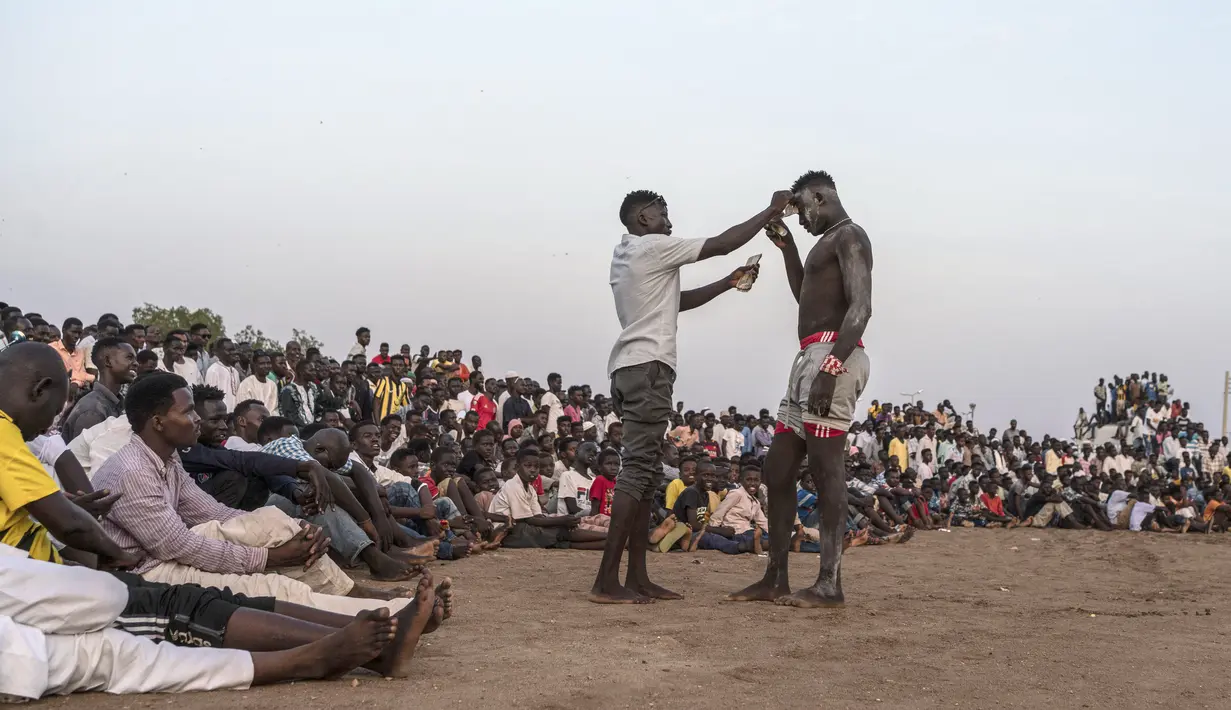 Seorang penonton menawarkan tip uang tunai kepada pegulat saat kompetisi gulat tradisional Nuba antara tim dari daerah Haj Youssef dan Omdurman di Ibu Kota Khartoum, Sudan, 30 Juli 2021. (Abdulmonam EASSA/AFP)