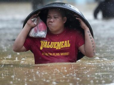 Seorang warga menggunakan bak cucian untuk melindunginya dari hujan saat ia menyeberangi jalan yang banjir akibat Badai Tropis Yagi, yang secara lokal disebut Enteng, di Cainta, provinsi Rizal, Filipina, Senin (2/9/2024). (AP Photo/Aaron Favila)