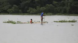 Seorang pria dan anak melakukan perjalanan dengan papan kayu melalui air banjir di daerah Bagha di Sylhet, Bangladesh (23/5/2022). Banjir bandang pra-musim telah membanjiri bagian dari India dan Bangladesh, menewaskan sedikitnya 24 orang dalam beberapa pekan terakhir dan mengirim 90.000 orang ke tempat penampungan. (AP Photo)