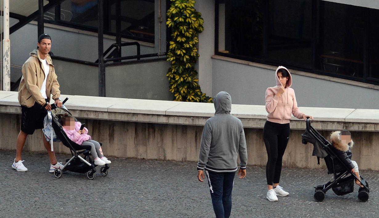 Cristiano Ronaldo bersama kekasihnya Georgina Rodriguez mengajak anak-anaknya berjalan santai di Funchal, Portugal, Sabtu (28/3/2020). Bintang Juventus ini memilih pulang kampung saat Serie A dihentikan sementara karena wabah virus corona. (AFP/Helder Santos)