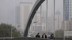 Orang-orang yang memakai masker untuk membantu mengekang penyebaran virus corona berjalan di atas jembatan di atas gedung perkantoran yang diselimuti kabut polusi di Beijing, Kamis (18/11/2021).  (AP Photo/Andy Wong)