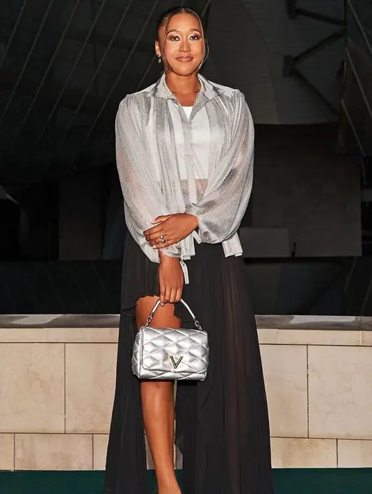 Naomi Osaka hadir mengenakan atasan kemeja silver transparan senada dengan tasnya. Dipadukan rok hitam asimetris. [Louis Vuitton]