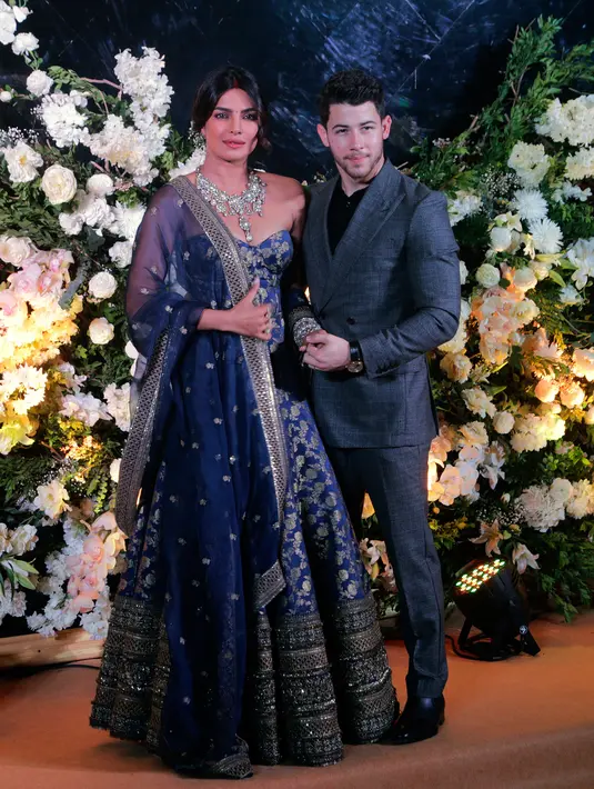 Pasangan aktris Bollywood Priyanka Chopra dan musisi Nick Jonas berpose untuk resepsi kedua pernikahan mereka di Mumbai, India, Rabu (19/12). Nick Jonas tampil klasik dan chic mengenakan setelan biru tua dan kemeja hitam. (AP/Rajanish Kakade)