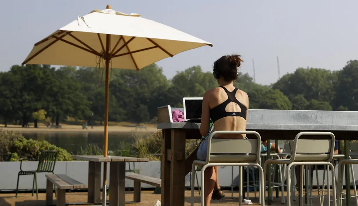 Seorang wanita menggunakan laptop saat dia duduk di luar di sebuah kafe di Hyde Park di London, Rabu, (12/8/20020). Peringatan badai masih berlaku untuk sebagian besar Inggris pada hari Rabu, sementara suhu tinggi diperkirakan lagi di banyak bagian Inggris. ( AP Photo / Kirsty Wigglesworth)