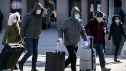 Wisatawan mengenakan masker berjalan dengan membawa barang bawaan mereka di Stasiun Kereta Api Beijing di Beijing, Kamis (28/1/2021).  Stasiun kereta api utama Beijing sebagian besar sepi pada hari pertama kesibukan perjalanan dan perkiraan jumlah penumpang lebih kecil daripada tahun-tahun sebelumny
