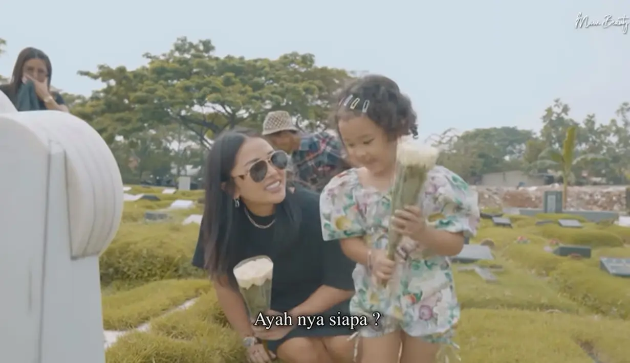 Turun dari mobil, Gewa tampak digandeng oleh sang ibu. Sedangkan tangan kirinya memegang bunga. Meski baru pertama turun, Gewa tampak sudah tahu makam sang ayah. [Youtube/Mutia Ayu]