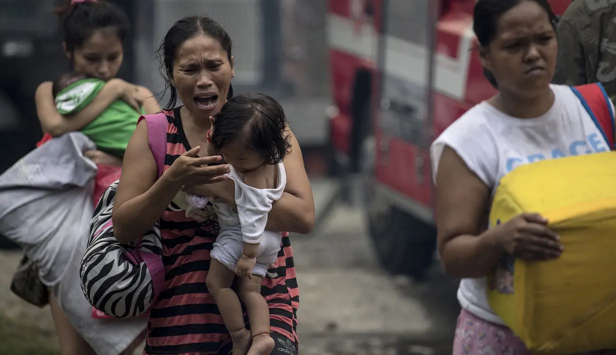 Warga membawa anak mereka mengungsi saat kebakaran melanda rumahnya di Manila, Filipina (11/8). Sejauh ini kebakaran menghancurkan 300 rumah dan mengakibatkan 800 keluarga harus dievakuasi. (AFP Photo/Noel Celis)