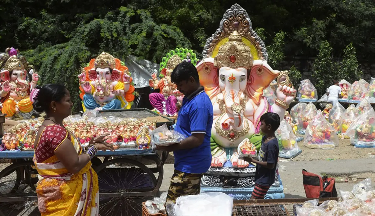 Seorang anak membantu orangtuanya menjual patung Dewa Ganesha di kios pinggir jalan di Hyderabad, India, Kamis (9/9/2021). Patung dewa Hindu berkepala gajah tersebut banyak dijual jelang Festival Ganesh Chaturthi. (NOAH SEELAM/AFP)