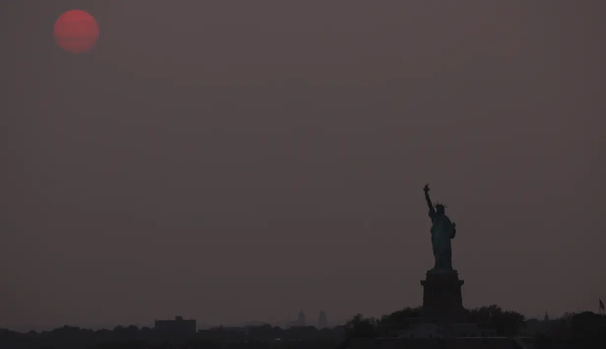 <p>Matahari terbenam di atas Patung Liberty di New York City, Amerika Serikat pada 22 Mei 2023. (Spencer Platt/Getty Images/AFP)</p>