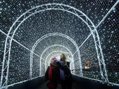 Pengunjung berjalan melewati terowongan yang dipenuhi cahaya lampu di Kew Gardens, London (21/11). Jelang perayaan Natal, Kew Gardens atau The Royal Botanical Garden dihiasi seni intalasi cahaya. (AP Photo/Frank Augstein)