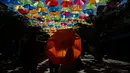 Seorang wanita berjalan menggunakan payung di bawah instalasi seni Umbrella Sky di Coral Gables, Florida, 16 Juli 2018. Coral Gables ini kota ketiga di AS yang menjadi tuan rumah bagi instalasi seni yang berlangsung hingga Agustus. (AP/Brynn Anderson)