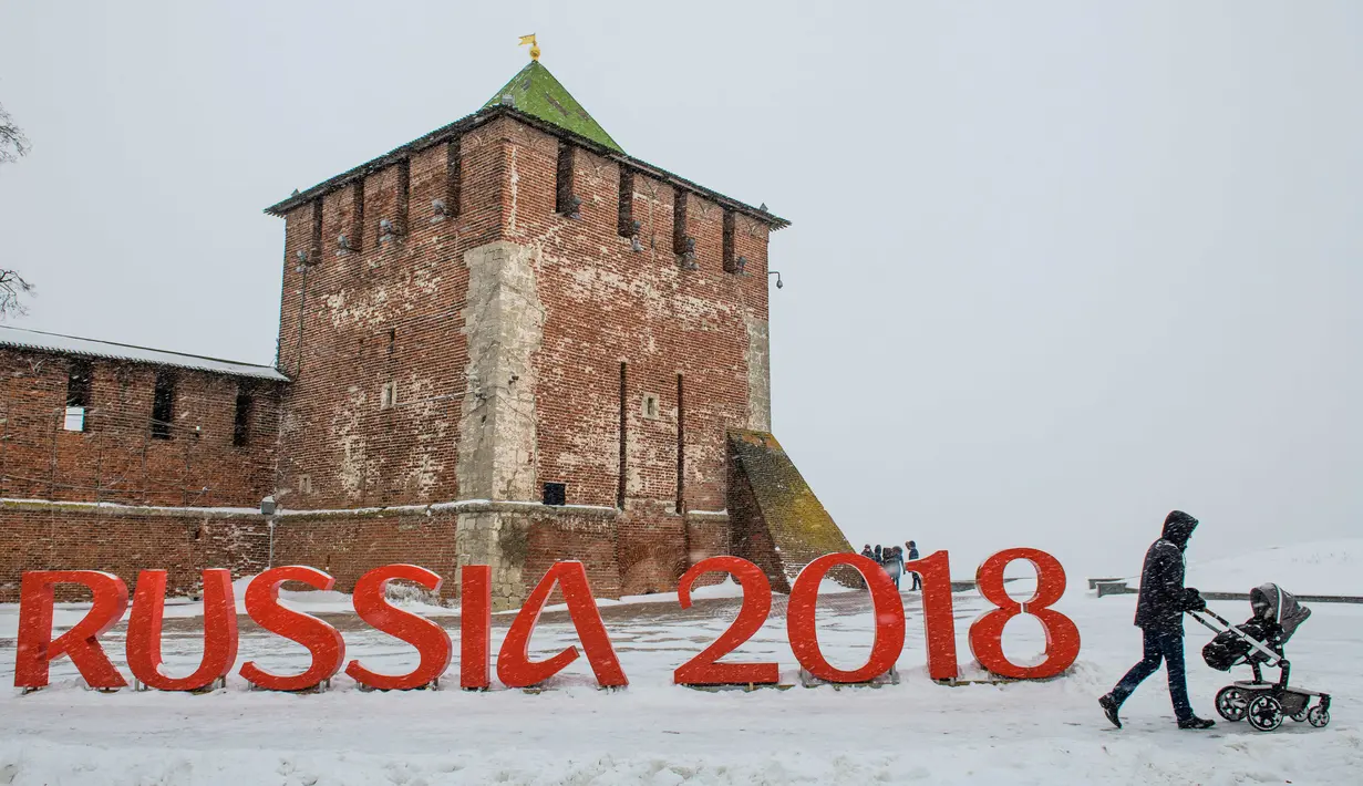 Seorang pria mendorong kereta dorong melewati lambang Piala Dunia 2018 yang ditempatkan di depan Kremlin, Nizhny Novgorod, Rusia, (21/1). Rusia akan menjadi tuan rumah Piala Dunia 2018. (Mladen ANTONOV/AFP)