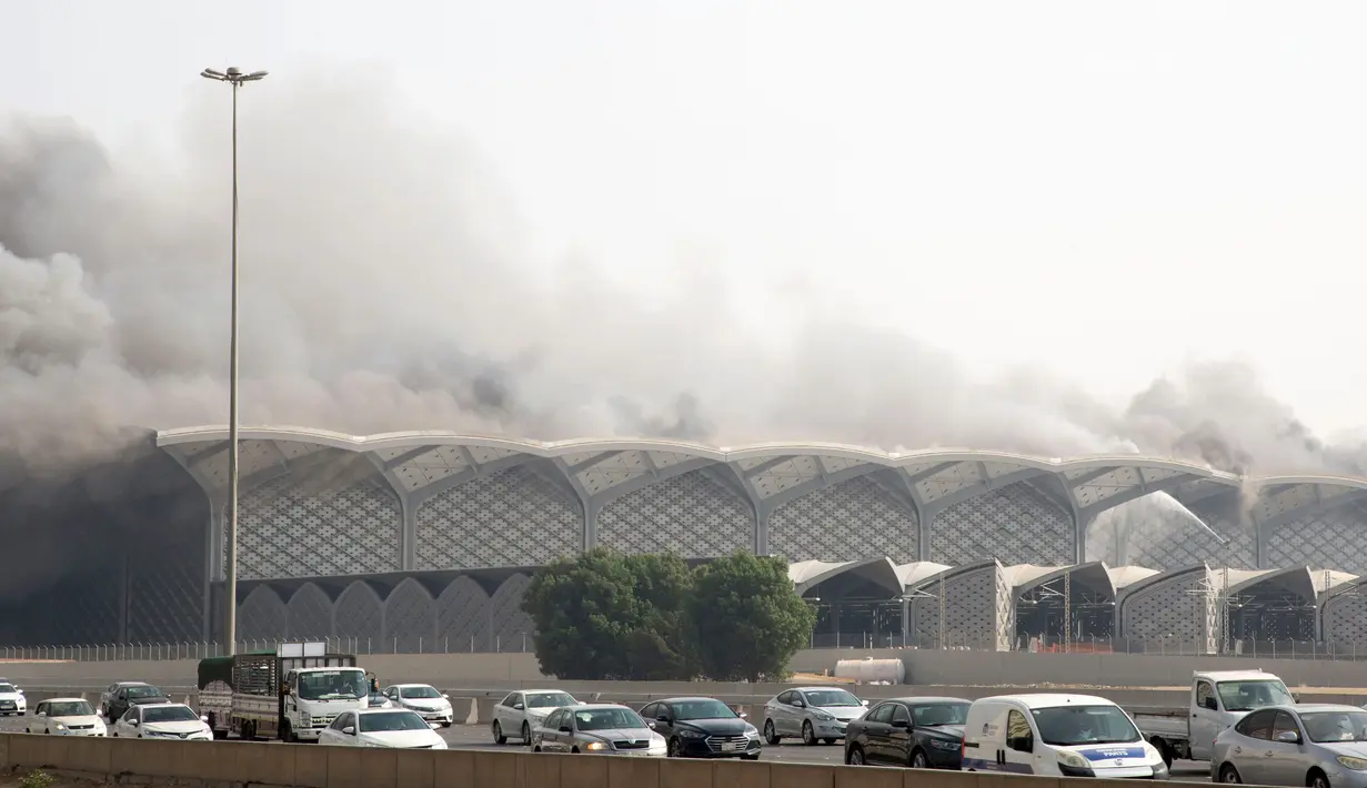 Mobil-mobil melaju saat asap hitam  membumbung menyelimuti gedung Stasiun Kereta Api Cepat Haramain di kota Jeddah, Minggu (29/9/2019). Pasukan Pertahanan Sipil Arab Saudi, dengan dukungan helikopter, harus berjuang selama berjam-jam untuk memadamkan api. (Photo by - / AFP)