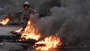 Seorang anak laki-laki melompati ban yang dibakar untuk memblokir jalan, selama protes di Beirut, Selasa (2/3/2021). Warga Lebanon yang marah memblokir jalan di seluruh negeri dengan membakar ban dan tempat sampah setelah mata uang Lebanon jatuh ke titik terendah baru. (AP Photo/Hassan Ammar)
