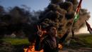 Warga Palestina membakar ban dan mengibarkan bendera nasional saat protes terhadap serangan militer Israel terhadap kamp pengungsi Jenin di perbatasan Israel-Palestina, sebelah timur Kota Gaza, 26 Januari 2023. Brigade Martir Al Aqsa, milisi bersenjata yang berafiliasi dengan Fatah mengatakan, salah satu anggotanya bernama Izz al-Din Salahat turut menjadi korban tewas. (AP Photo/Fatima Shbair)