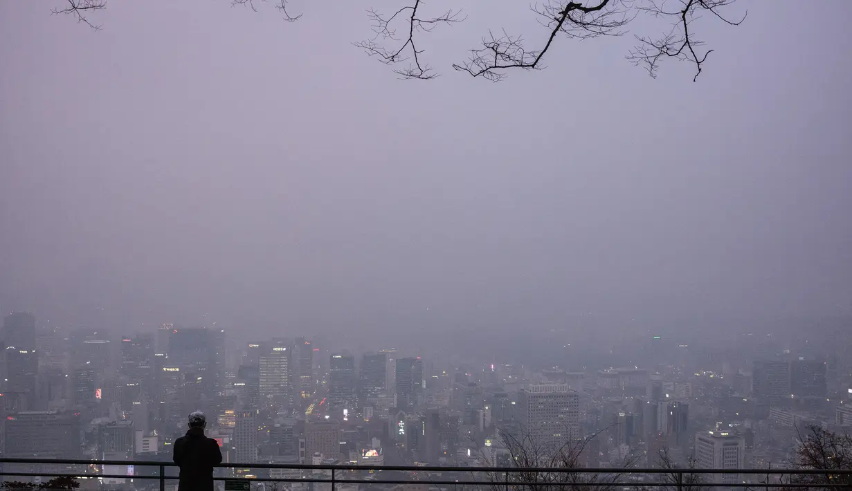 Seorang pria melihat ke arah gedung-gedung yang diselimuti kabut saat ia mengunjungi Menara Namsan pada hari yang tercemar di Seoul, Korea Selatan, Rabu (15/12/2021). (AFP/Anthony Wallace)