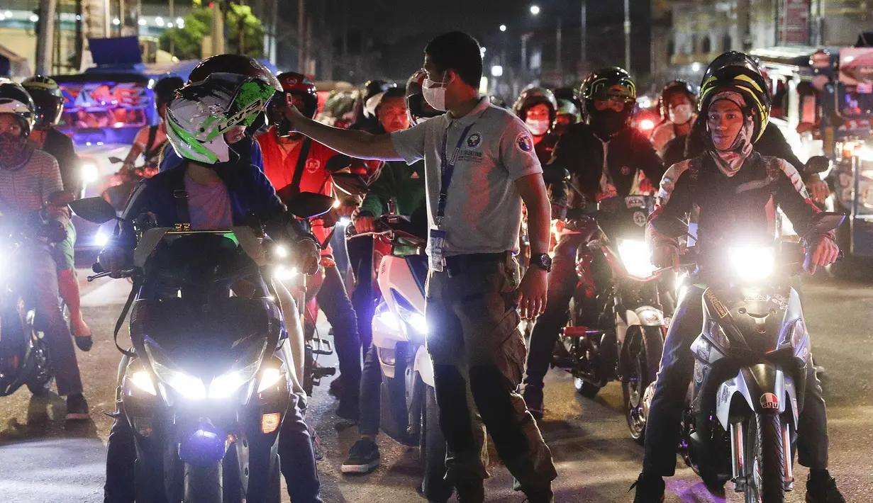 Petugas lalu lintas memeriksa suhu tubuh pengendara sepeda motor di pos pemeriksaan virus corona COVID-19 di Manila, Filipina, Senin (16/3/2020). Polisi beserta petugas lalu lintas dan petugas desa mengecek suhu tubuh warga untuk mencegah penyebaran virus corona COVID-19. (AP Photo/Aaron Favila)