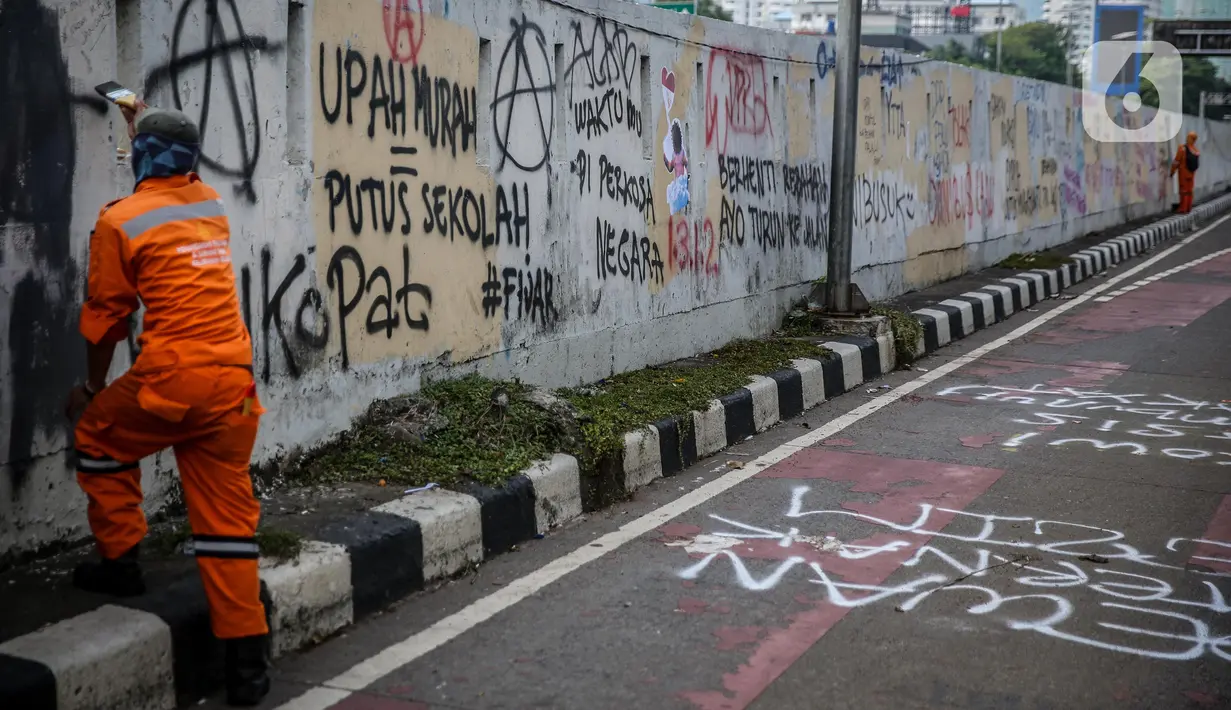 Petugas PPSU membersihkan coretan yang mengotori pembatas jalan pascaunjuk rasa di kawasan DPR/MPR, Jakarta, Jumat (17/7/2020). Coretan tersebut dilakukan oleh massa yang menolak RUU Omnibus Law Cipta Lapangan Kerja di depan Gedung DPR pada Kamis (16/7) kemarin. (Liputan6.com/Faizal Fanani)