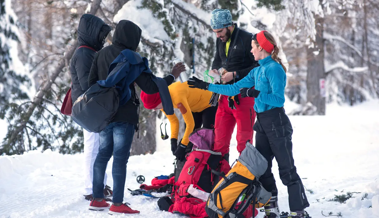 Turis Prancis menawarkan makanan dan minuman kepada para imigran dari Pantai Gading yang berjalan diatas salju untuk menuju perbatasan antara Italia dan Prancis di Pegunungan Alpen, Italia (13/1). (AFP/Piero Cruciatti)