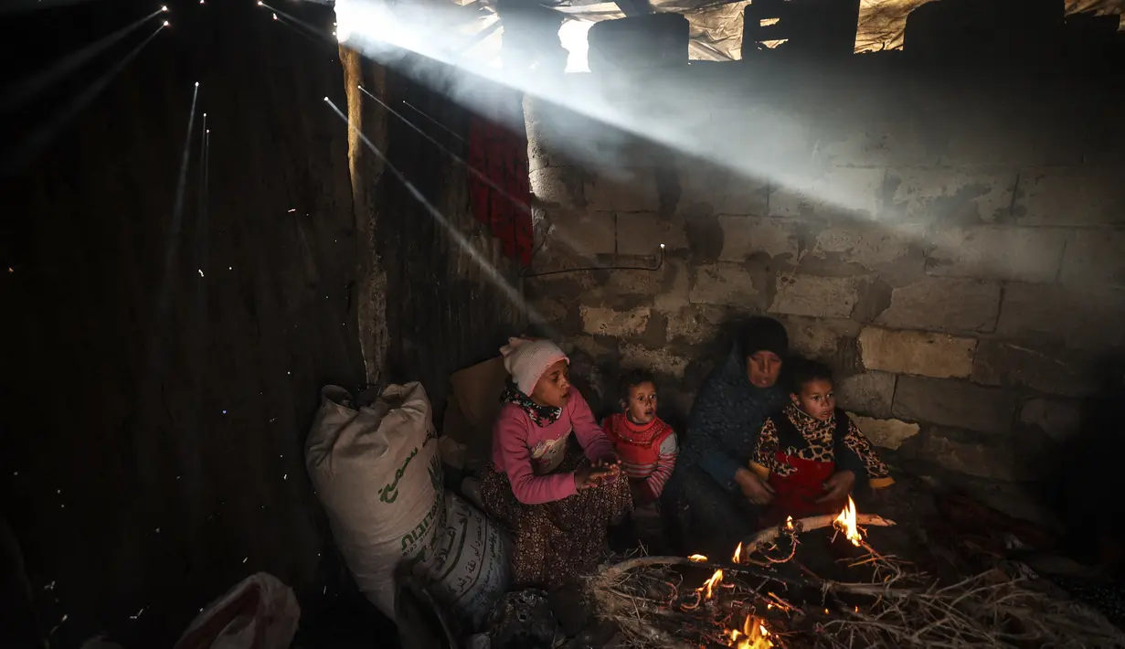 Sebuah keluarga Palestina menghangatkan diri di sebelah api pada hari hujan di Khan Yunis, di Jalur Gaza selatan pada 19 Januari 2022. (Mahmud HAMS / AFP)