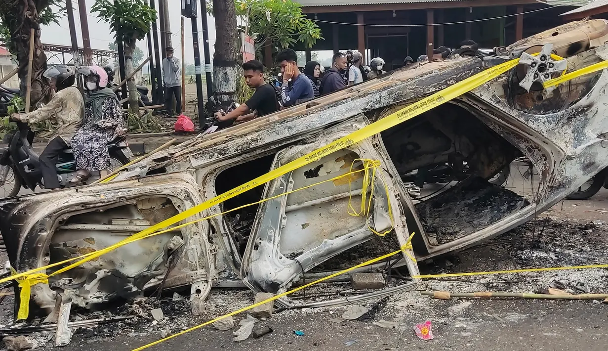 Pengendara melewati puing-puing mobil yang terbakar dalam kerusuhan di luar Stadion Kanjuruhan, Malang, Jawa Timur, Minggu (2/10/2022). Sebanyak 127 orang tewas ketika para penggemar yang marah menyerbu lapangan sepak bola setelah pertandingan antara Arema FC dan Persebaya Surabaya pada 1 Oktober 2022. (AP Photo/Hendra Permana)