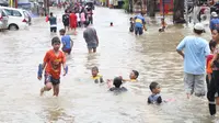 Anak-anak bermain di genangan air yang membanjiri Jalan KH Hasyim Ashari, Tangerang, Banten, Kamis (2/1/2020). Banjir yang menggenangi jalan penghubung Jakarta- Tangerang tersebut mulai surut dan sudah bisa dilintasi pejalan kaki. (Liputan6.com/Angga Yuniar)