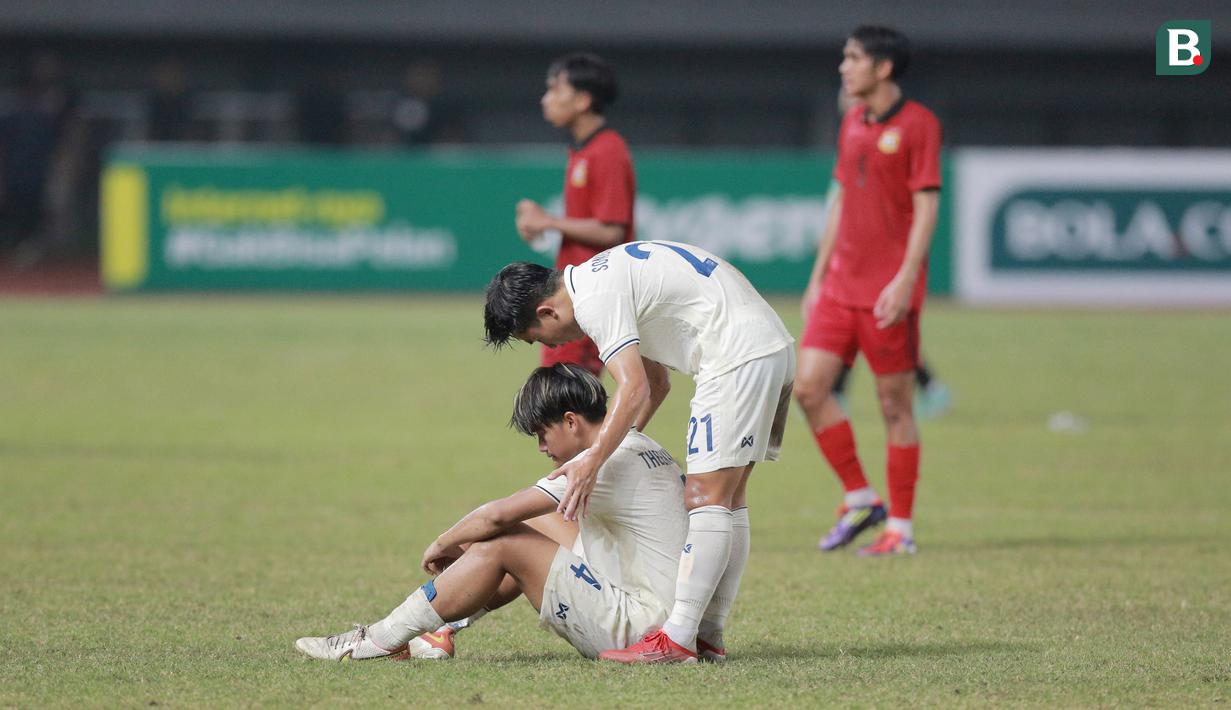 Pemain Thailand U-19, Songkhramsamut Namphueng berusaha membangunkan Theekawin Chansri yang terduduk lesu usai ditaklukkan Laos U-19 pada laga semifinal Piala AFF U-19 2022 di Stadion Patriot Candrabhaga, Bekasi, Rabu (13/7/2022). (Bola.com/M Iqbal Ichsan)