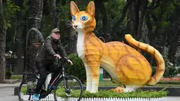 Foto yang diambil pada 16 Januari 2023 ini menunjukkan seorang pria mengendarai sepeda melewati patung kucing di Taman Thong Nhat di Hanoi, menjelang tahun baru Imlek. Tak ada penjelasan resmi mengapa masyarakat Vietnam mengadopsi kucing sebagai hewan keempat dalam astrologi atau shio mereka dan bukannya kelinci seperti di China. (Nhac NGUYEN / AFP)