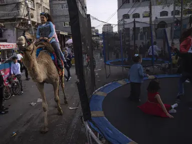 Gadis-gadis Palestina menunggang unta saat mereka merayakan festival Idul Fitri, menandai akhir bulan puasa Ramadhan di kamp pengungsi al-Shati, Jalur Gaza barat, Sabtu, 22 April 2023. (AP Photo/Fatima Shbair)