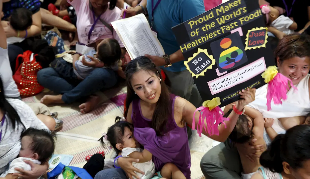 Seorang ibu menyusui anaknya sambil menunjukkan poster, di kota Mandaluyong, Filipina, Sabtu (1/8/2015). Dalam rangka memperingati Hari ASI Sedunia, mereka menggelar kegiatan menyusui yang disebut "Hakab Na 2015".  (REUTERS/Erik De Castro)