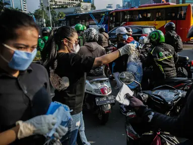 Relawan membagikan masker kepada pengguna jalan di Kawasan Bundaran HI, Jakarta, Selasa (17/3/2020). Sebanyak 3.000 masker dibagikan secara gratis sebagai salah satu bentuk keprihatinan sekaligus berpartisipasi dalam upaya mencegah penyebaran virus corona COVID-19. (Liputan6.com/Faizal Fanani)