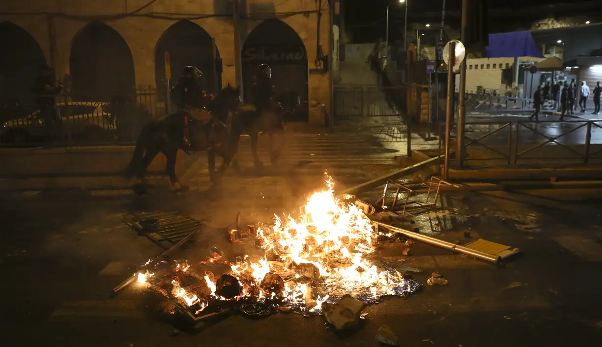 Petugas polisi Israel yang berkuda melewati api saat bentrokan dengan warga Palestina, tepat di luar Kota Tua Yerusalem, Kamis (22/4/2021).  Warga Palestina bentrok dengan polisi Israel atas pembatasan pertemuan Ramadhan. (AP Photo/Mahmoud Illean)