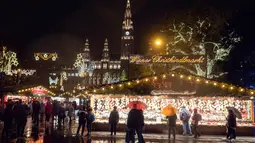 Wisawatan menerobos hujan saat mengunjungi pasar Natal di luar City Hall, Wina pada 26 November 2018. Christkindlmarkt menjadi ciri khas Natal dan musim dingin di Austria dan juga Jerman yang sudah sejak pertengahan tahun 1310. (JOE KLAMAR / AFP)