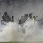 Petugas polisi dan tentara berdiri di tengah asap gas air mata setelah berusaha membubarkan penonton yang memasuki lapangan Stadion Kanjuruhan, Malang, Jawa Timur, Indonesia, Sabtu, 1 Oktober 2022. (AP/Yudha Prabowo)