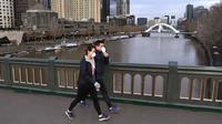 Orang-orang dengan masker berjalan di jembatan yang melintasi Sungai Yarra pada hari pertama wajib masker, di Melbourne Kamis (23/7/2020). Penduduk kota terpadat kedua di Australia, Melbourne, diwajibkan mengenakan masker saat meninggalkan rumah untuk mencegah penyebaran COVID-19. (William WEST/AFP)
