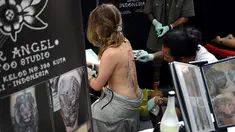 Seorang wanita saat dibuatkan tato dibagian punggung oleh seniman dalam acara Bali Tattoo Expo 2017 di pulau resor Indonesia, Denpasar, Bali (12/5). Acara ini digelar selama 3 hari, mulai (12/5/2017) sampai (14/5/2017). (AFP Photo/Sonny Tumbelaka)
