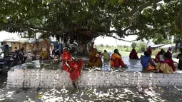 Sejumlah warga duduk berteduh pada pohon di tengah meningkatnya suhu di New Delhi, India, Selasa (26/5/2020). Saat ini India sedang mengalami hari-hari terpanas di bulan Mei selama hampir dua dekade terakhir. (Money SHARMA/AFP)