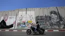 Seorang wanita mengambil gambar grafiti Presiden AS Donald Trump di tembok pemisah Israel - Palestina di kota Bethlehem (4/8).  (AFP Photo/Musa Al Shaer)