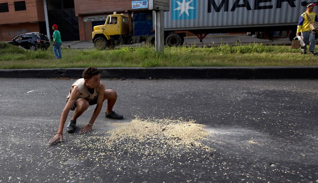 Seorang pemuda mengumpulkan biji-bijian jagung yang jatuh dari sebuah truk akibat dijarah di luar pelabuhan di Puerto Cabello, Venezuela, Selasa (30/1). Venezuela tengah menghadapi krisis ekonomi yang cukup parah. (AP Photo/Fernando Llano)