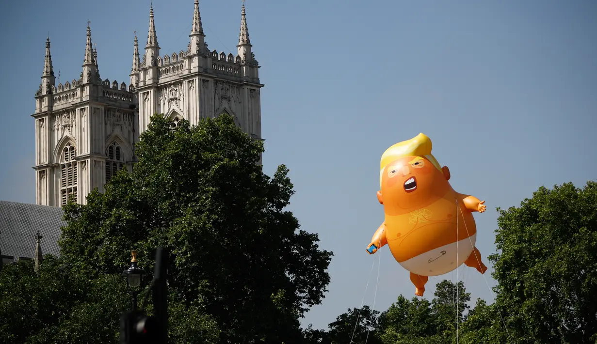 Balon raksasa berbentuk bayi menyerupai Presiden AS, Donald Trump melayang dekat menara Westminster Abbey selama demonstrasi di Parliament Square, London, Jumat (13/7). Puluhan ribu orang menggelar aksi damai menentang kedatangan Trump. (AFP/TolgaAKMEN)