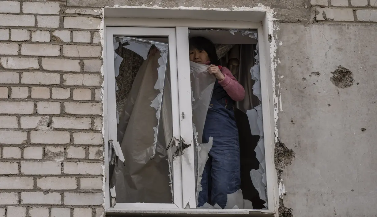 Seorang wanita meletakkan plastik di atas jendelanya yang rusak setelah serangan Rusia pada malam sebelumnya, di daerah perumahan Mikolaiv, Ukraina, 29 Maret 2022. Invasi Rusia ke Ukraina yang dimulai pada 24 Feberuari 2022 masih berlangsung hingga hari ini. (AP Photo/Petros Giannacouris)