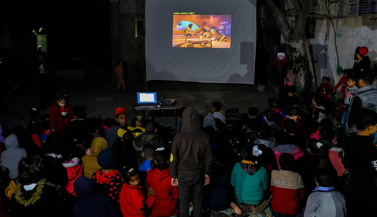 Anak-anak Palestina menonton sebuah film kartun yang ditayangkan pada layar putih berukuran besar yang dipasang di salah satu gang sempit di Kamp Pengungsi Nuseirat di Jalur Gaza tengah pada 26 Januari 2020. (Xinhua/Rizek Abdeljawad)