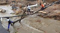 Warga berjalan melintasi jembatan darurat di atas sungai setelah sebuah jembatan hanyut di Ntuzuma, luar Durban, Afrika Selatan, 12 April 2022. Hujan berkepanjangan dan banjir di Provinsi KwaZulu-Natal Afrika Selatan telah merenggut nyawa setidaknya 20 orang, menurut pejabat setempat. (AP Photo/Str)