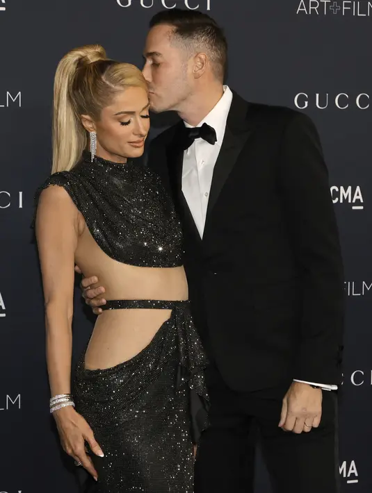 Paris Hilton dicium suaminya Carter Reum saat enghadiri LACMA ART+FILM GALA 2022 yang dipersembahkan Oleh Gucci di Los Angeles County Museum of Art di Los Angeles, California pada 5 November 2022. Mereka berpakaian apik dalam warna hitam dari ujung kepala hingga ujung kaki. (Kevin Winter/Getty Images/AFP)