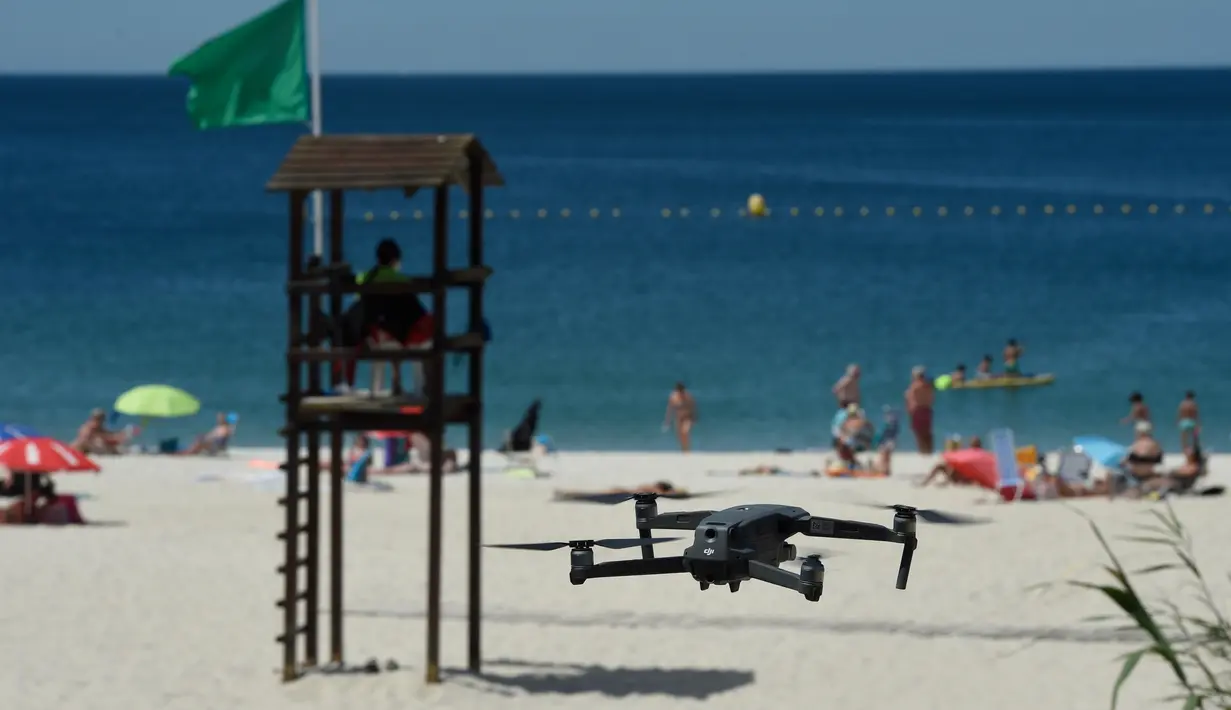 Sebuah drone atau pesawat tak berawak yang diterbangkan oleh polisi setempat memperingatkan orang-orang untuk menjaga jarak di pantai Areas di Sanxenxo, Spanyol, Selasa (14/7/2020). Drone tersebut untuk memantau jaga jarak antarwisatawan saat berlibur di masa pandemi Corona. (MIGUEL RIOPA / AFP)
